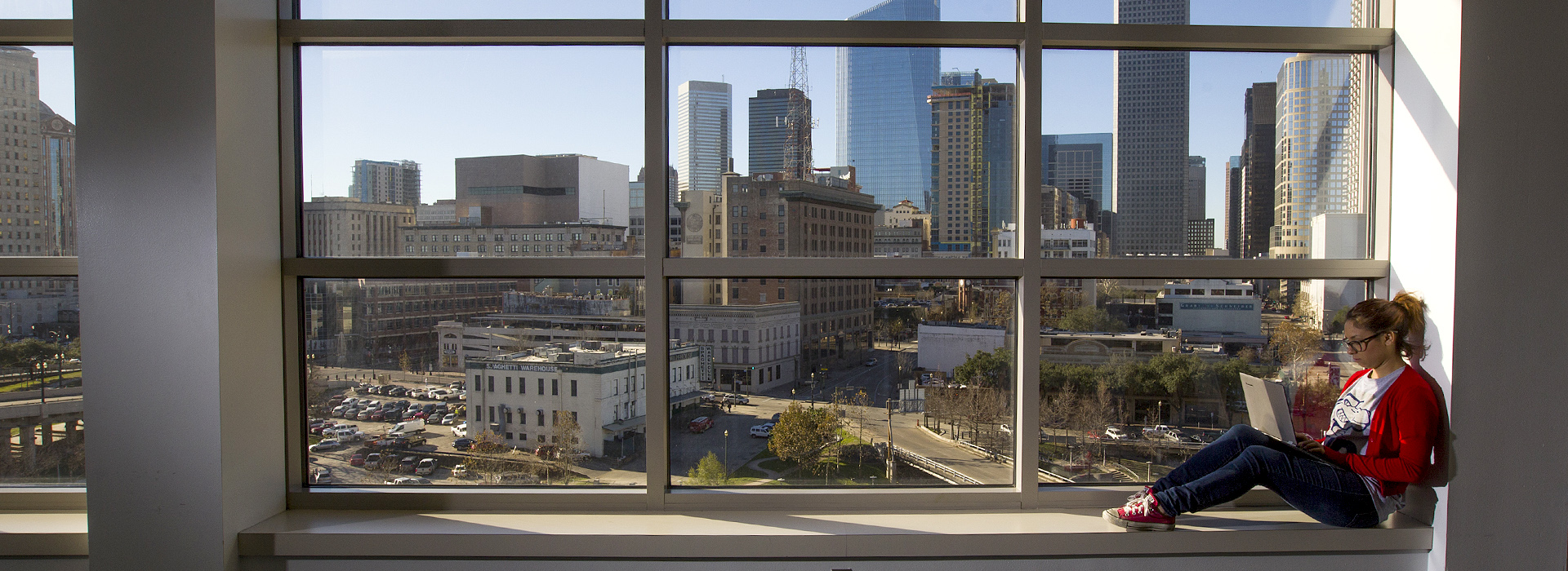 female student on a laptop sitting in a window in the UHD academic building