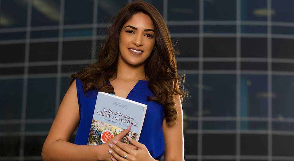 Student standing in front of glass holding a book.