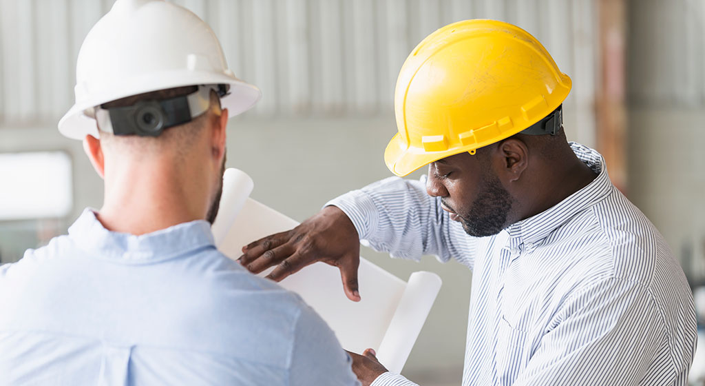 Two men in hard hats looking at blueprints.