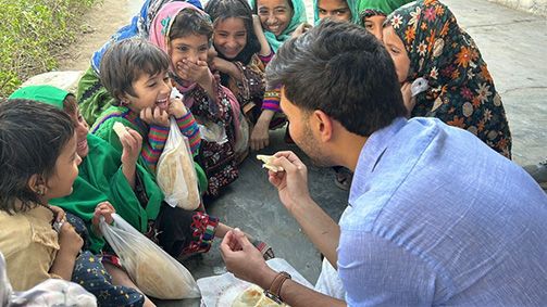 Ammar Ansari Psychology major and senior at the university of houston-downtown holds a piece of flat bread while children laugh and smile around him 