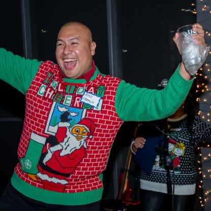 UHD alum, a bald man in a holiday sweater with Santa on it (Santa is waving) celebrates winning a prize.