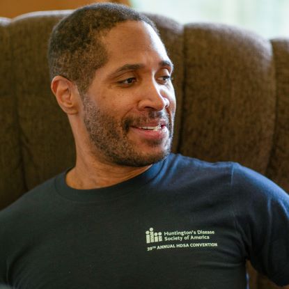 Patrick Caballero wears a blue shirt and sits in a brown chair.