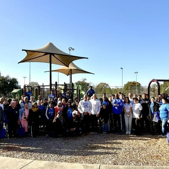 A group of UHD faculty, staff, and students pose for a group photo at Moody Park in front of a playground. The sky overhead is clear and blue.