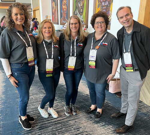 Diane Miller, Stephen Winton, Sarah Albrecht, and Kim Pinkerton and Kelly Tumy wear conference lanyards and smile 