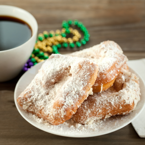New orleans style beignets, a cup of coffee, and mardi gras beads