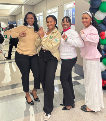 Four members of a greek organization wear branded clothing and hold up sorority hand signs during university of houston-downtown's week of welcome 
