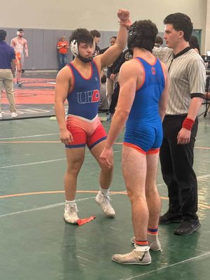 Two university of houston-downtown students and members of the wrestling team with a referee. the referee holds up one of the student's arms.