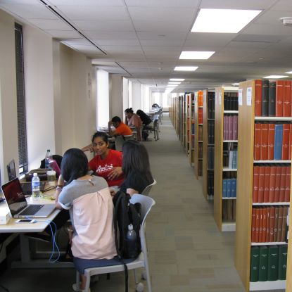 Library shelves with students opposite them, speaking to each other.