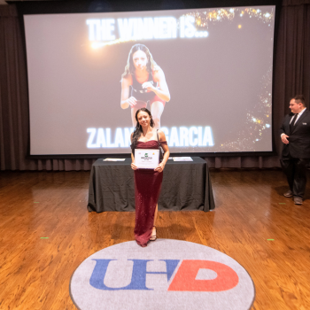 UHD athlete on wrestling team wears a long formal gown and holds an awards certificate at UHD's One Main Event