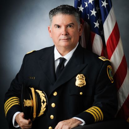 Chief Diaz poses for a photo in a formal police uniform. The american flag is behind him.