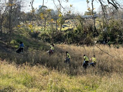 Students pick up trash at Moody Park. They wear neon vests.