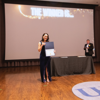 A UHD student wearing a long formal gown holds an award certificate 