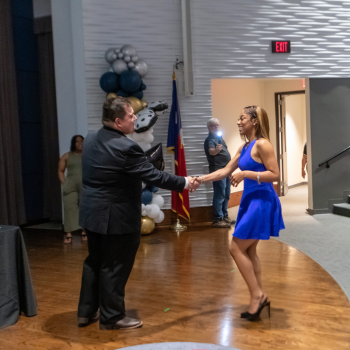 A UHD student in a blue formal dress shakes hands with UHD staff member and Esports Coordinator