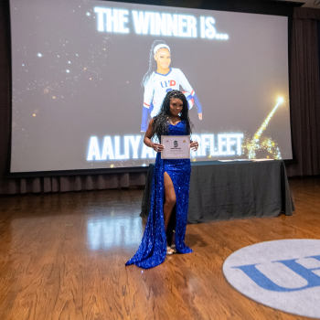 A UHD volleyball player in a blue gown holds an award certificate at the UHD sports and fitness awards 