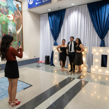 UHD Marilyn Davies College of Business students pose in front of a lit Marquee while an individual takes a photo 