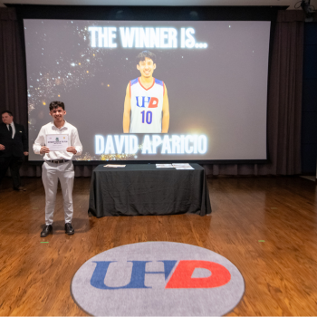 UHD student basketball player holds an award certificate on stage