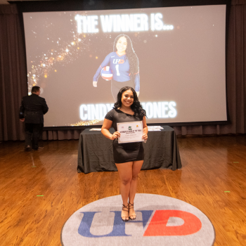A UHD student volleyball player in a black dress holds a sports and fitness award certificate